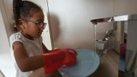 young child washing dishes with water coming out of sink faucet
